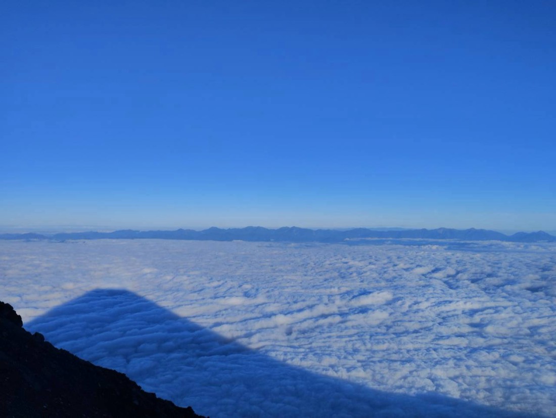 富士山頂から見た雲海と影富士、遠くに南アルプス